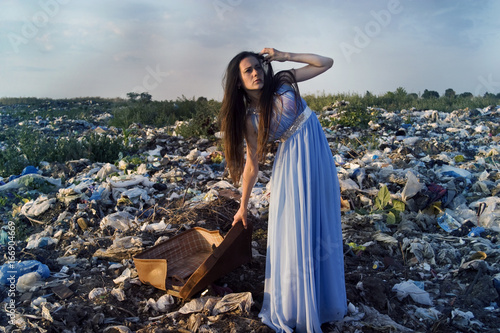 A girl with a suitcase on a garbage dump directed her gaze into the distance