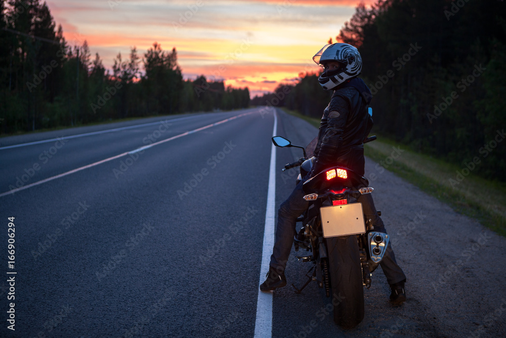 Motorcycle driver sitting on bike and turning to camera from back at night time, roadside Motorcycle driver sitting on bike and turning to camera from back at night time, roadside
