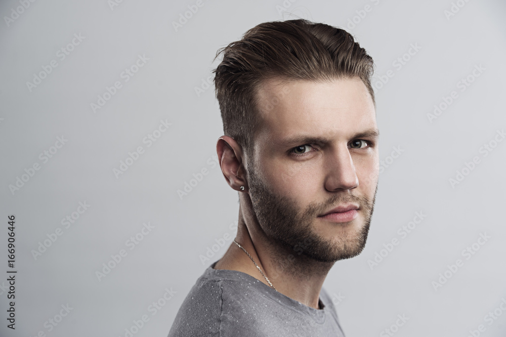 Fototapeta premium Close up portrait of serious gloomy bearded man with stylish hairstyle posing against white background. Handsome guy with blue eyes frowning his face showing his disatisfaction and dipleasment