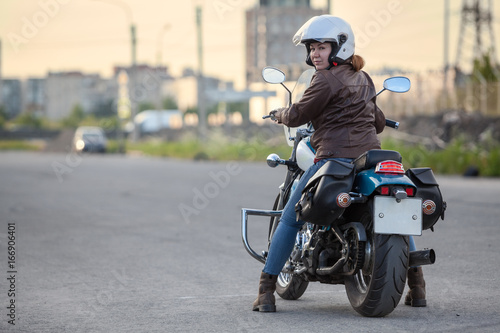 Woman a motorcyclist looking back when standing on motorbike on asphalt road, copy space