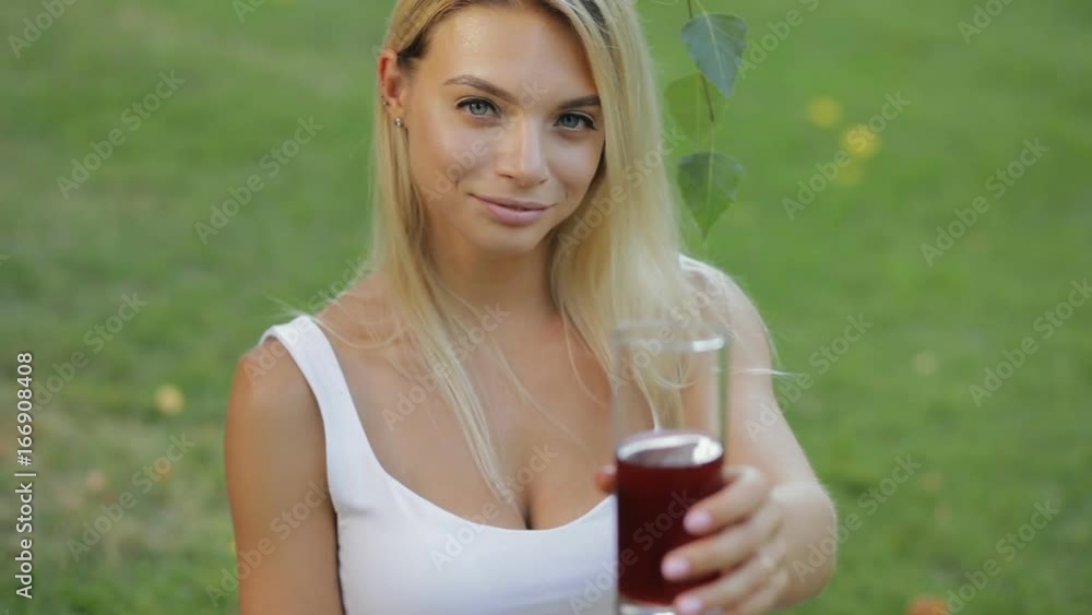 Healthy lifestyle drink. Young woman give a garnet juice sitting outdoors at meadow in slow motion Healthy lifestyle drink. Young woman give a garnet juice sitting outdoors at meadow in slow motion