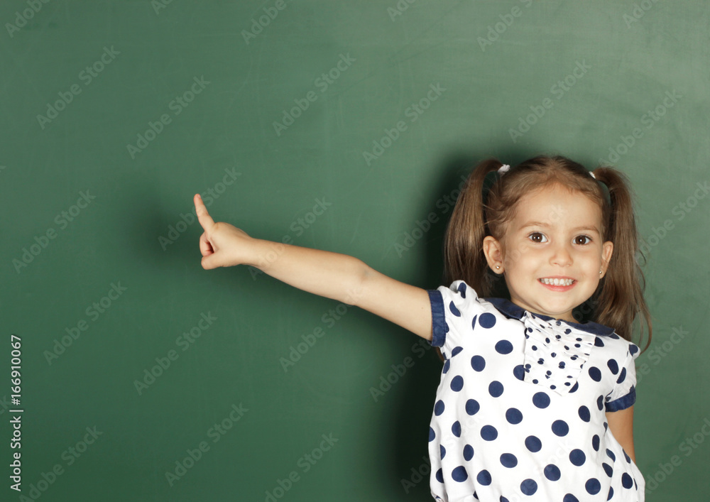 Smiling child girl show with a finger blank school blackboard, copy space Smiling child girl show with a finger blank school blackboard, copy space
