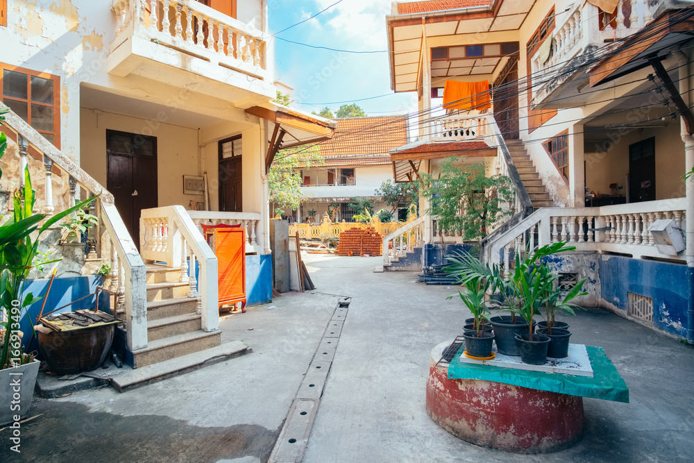Obraz premium Old traditional street in Bangkok - one of the popular attractions for tourists in Thailand. City view of small rural road with houses, green lush trees and everyday lifestyle atmosphere at sunny day