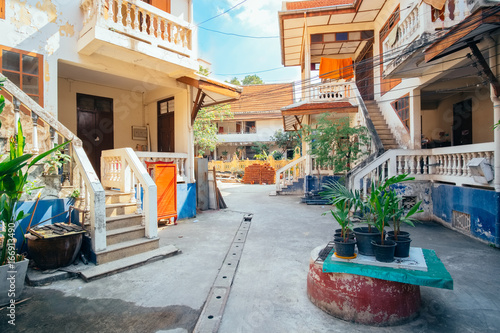 Fototapeta Naklejka Na Ścianę i Meble -  Old traditional street in Bangkok - one of the popular attractions for tourists in Thailand. City view of small rural road with houses, green lush trees and everyday lifestyle atmosphere at sunny day
