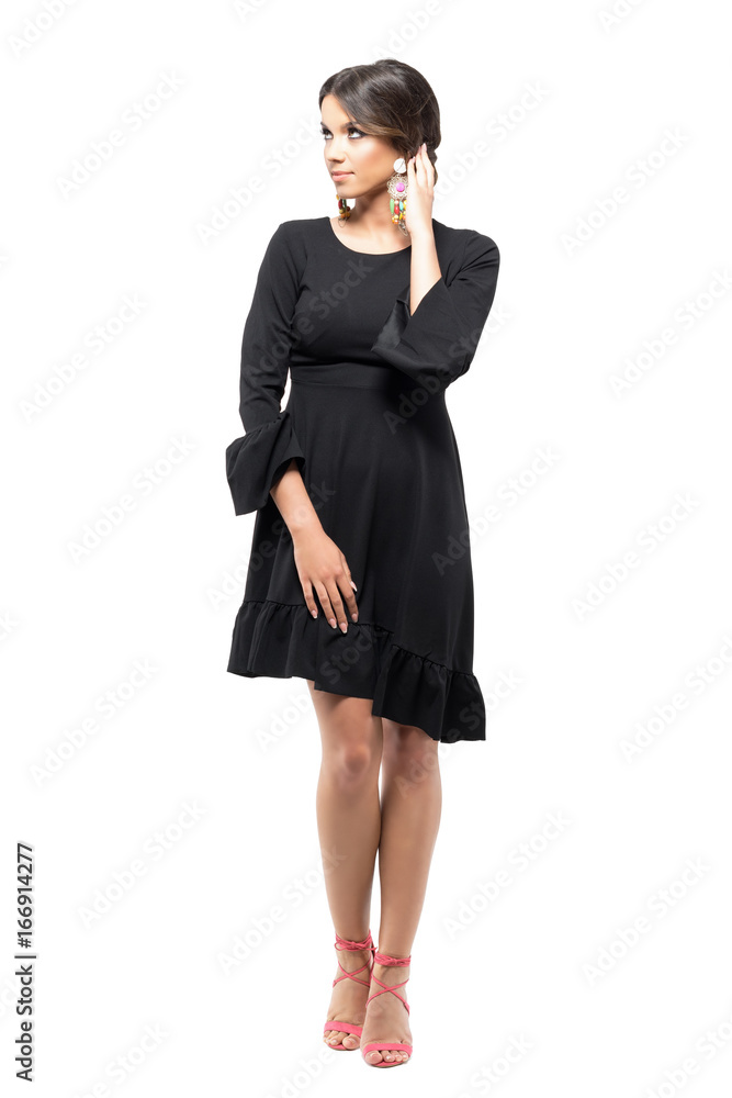 Beautiful Latin tanned woman in black dress touching and adjusting hair looking up.  Full body length portrait isolated on white studio background.