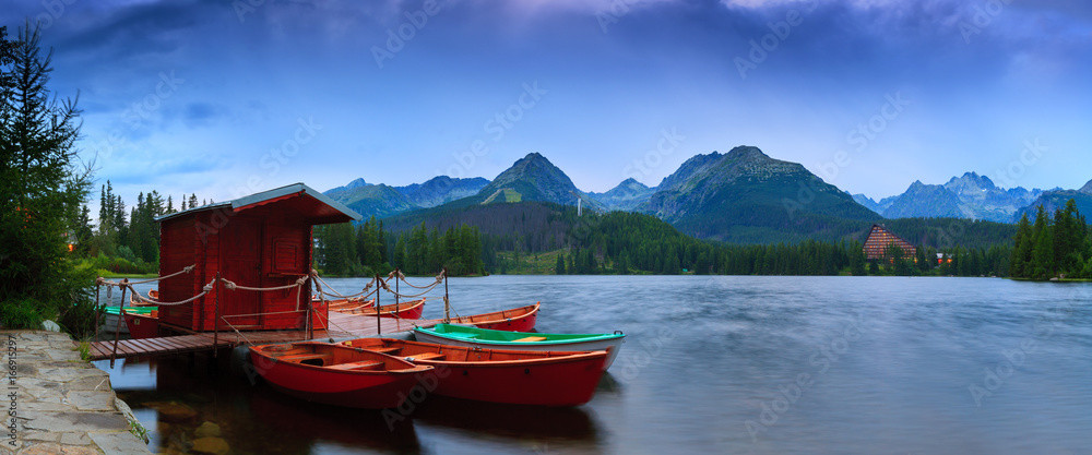 Panoramic picture of beautiful mountain lake Strbske Pleso at summer evening. Moored boats on pier. High Tatras. Slovakia. Panoramic picture of beautiful mountain lake Strbske Pleso at summer evening. Moored boats on pier. High Tatras. Slovakia.