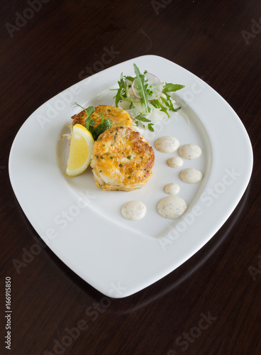 Beautiful fresh golden fish cakes, served with a wedge of lime, dill sauce and rocket on a white plate