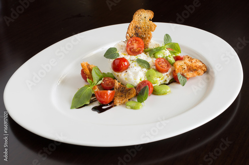 Delicious tomato and mozzarella cheese salad caprese, served on a white plate, with basil, croutons and balsamic vinegar. photo