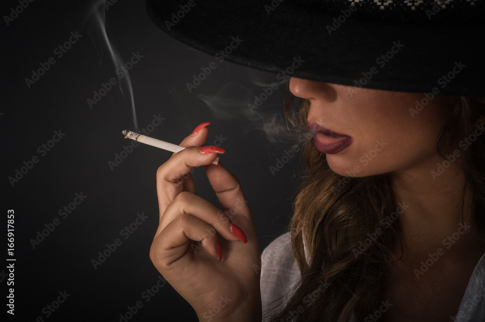 Fototapeta premium Portrait of sexy elegant lady woman with hat smoking cigarette