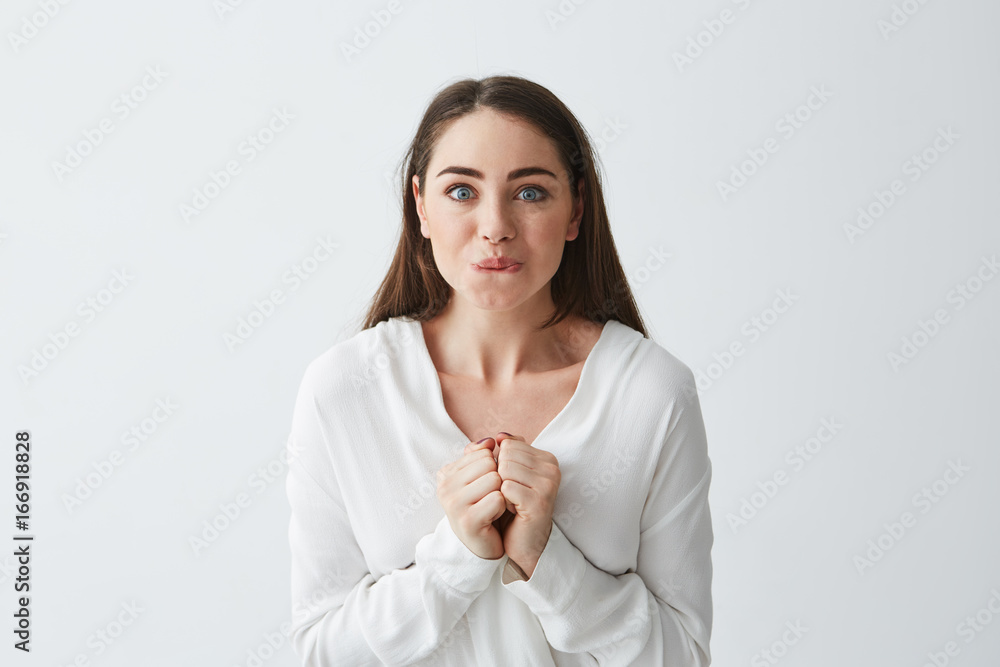 Happy excited young business woman looking at camera biting lips holding jaws over white background.