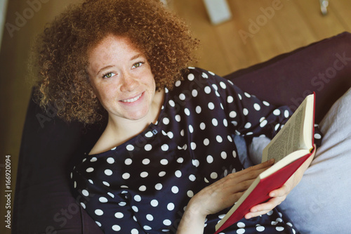 jeune femme rousse souriante lisant un livre