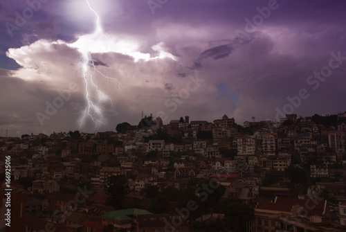 Tropical storm, thunderstorm, rain. Lightning above the city in the night violet sky