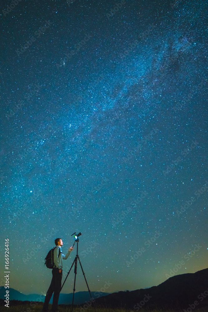 Obraz premium The man with a camera stand on the background of the starry sky. night time