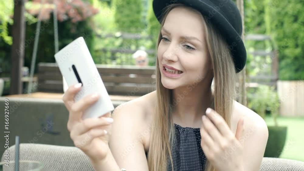 Pretty girl in bowler hat doing selfies on smartphone in the cafe's garden, steadycam shot
Pretty girl in bowler hat doing selfies on smartphone in the cafe's garden, steadycam shot