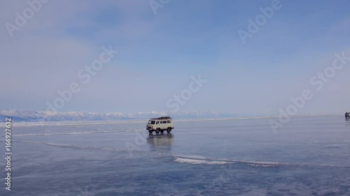 Frozen lake Baikal covered with snow and ice. Cars drive over the ice. Aerial view. Flying around 4k