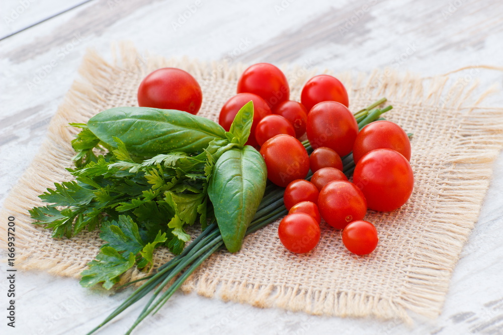 Red cherry tomatoes with green parsley and basil on jute canvas Red cherry tomatoes with green parsley and basil on jute canvas