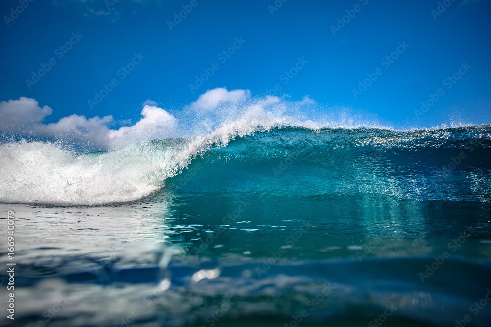 Front view of Big ocean wave in daylight. Blue sky with clouds. .Sea swell for surfing sport activity. Nobody on picture. Vibrant bright tropical colorful image with copy space on a water surface.