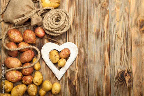 Raw potatoes, bag and heart on a wooden table