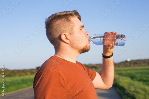 Bilde på lerret Closeup portrait of young guy drinking water from bottle on a hot sunny day