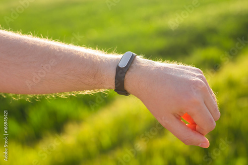 Sport, gadget, activity tracker and people concept - Close up of runner jogging outside looking at his wearable fitness bracelet.