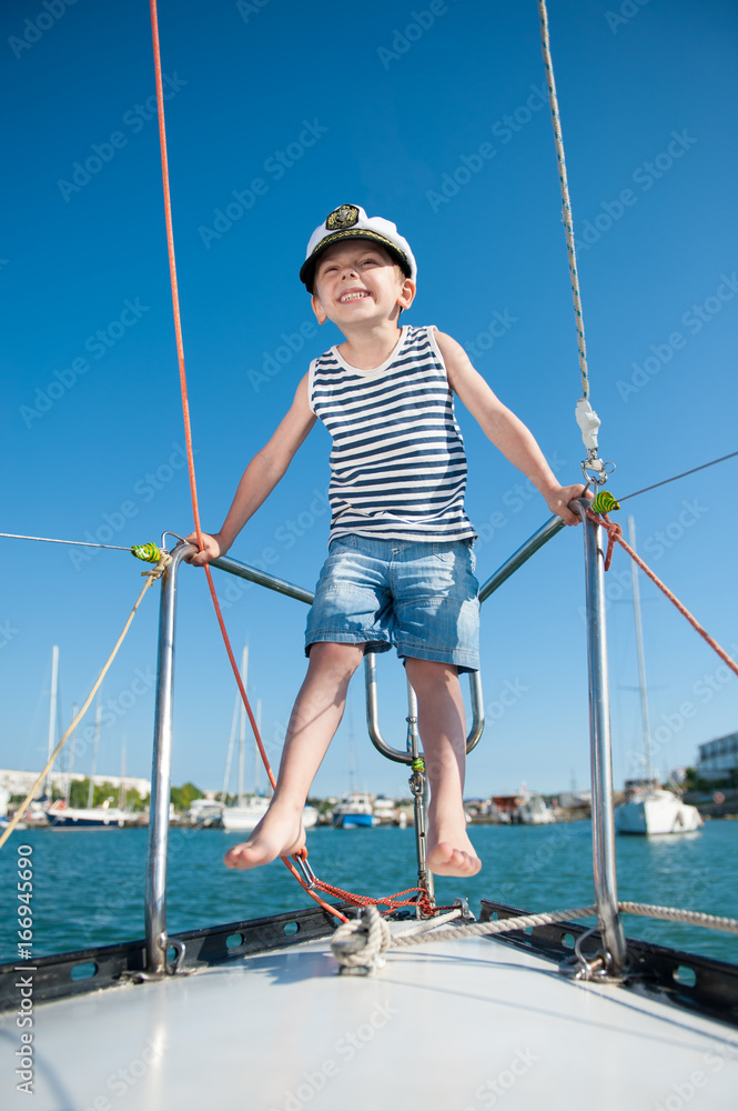 happy small boy wearing captain cap on luxury white yacht in summer day