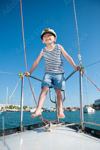 happy small boy wearing captain cap on luxury white yacht in summer day
