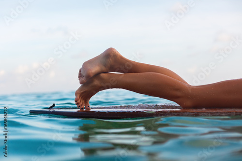 Happy girl in bikini have fun before surfing Surfer lie on surf board. Close up bare legs. People in water sport adventure camp, extreme activity on family summer beach vacation. Watersport background
