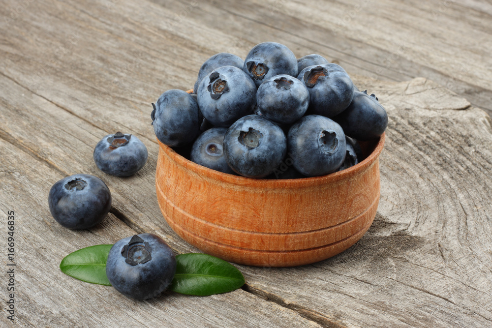 blueberries with green leaf in wooden bowl on old wooden table background blueberries with green leaf in wooden bowl on old wooden table background
