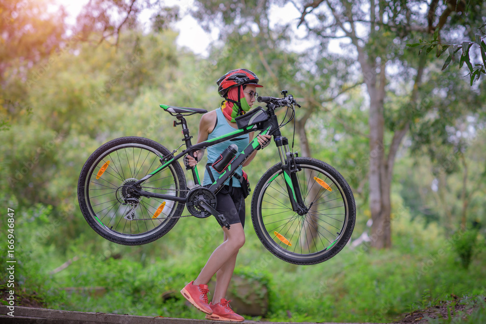 woman carry mountain bike by holding frame body of bicycle cross over raceway in the rainforest
