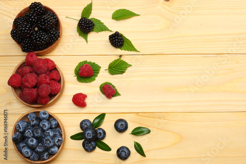 mix of blueberries  blackberries  raspberries in wooden bowl on light wooden table background. top view with copy space