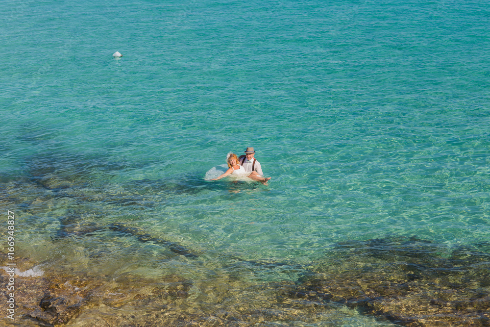Happy couple swims after wedding in turquoise sea. Romantic newly-married couple enjoying a summer vacation.