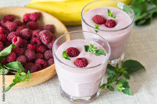 Two glasses of smoothies from banana and raspberries on a background of fruit