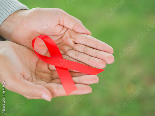 Closeup female hands holding red ribbon HIV  world AIDS day awareness ribbon.  Healthcare and medicine concept.