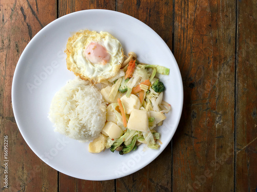 Stir-fried mixed vegetables with tofu and fried egg with rice in white dish on wooden background.  Vegetarian Food, healthy food.