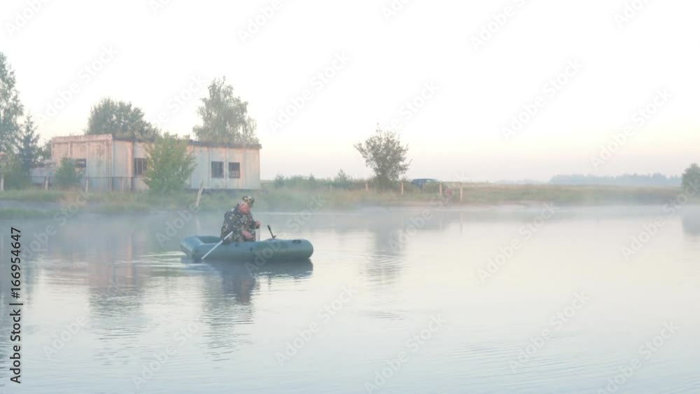 Inflatable boat with a male fisherman on a lake in the fog. Early morning. Inflatable boat with a male fisherman on a lake in the fog. Early morning.