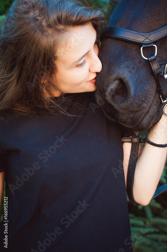 Emotional Portrait of a female in love with horses, black Friesian stallion thoroughbred pet, outdoors.