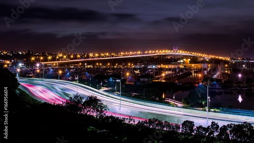 Time lapse of cars in motion on a lighted bridge and highway over the sea with anchored sailing boats at westhaven marina of Auckland in New Zealand with a cloudy and starry sky photo