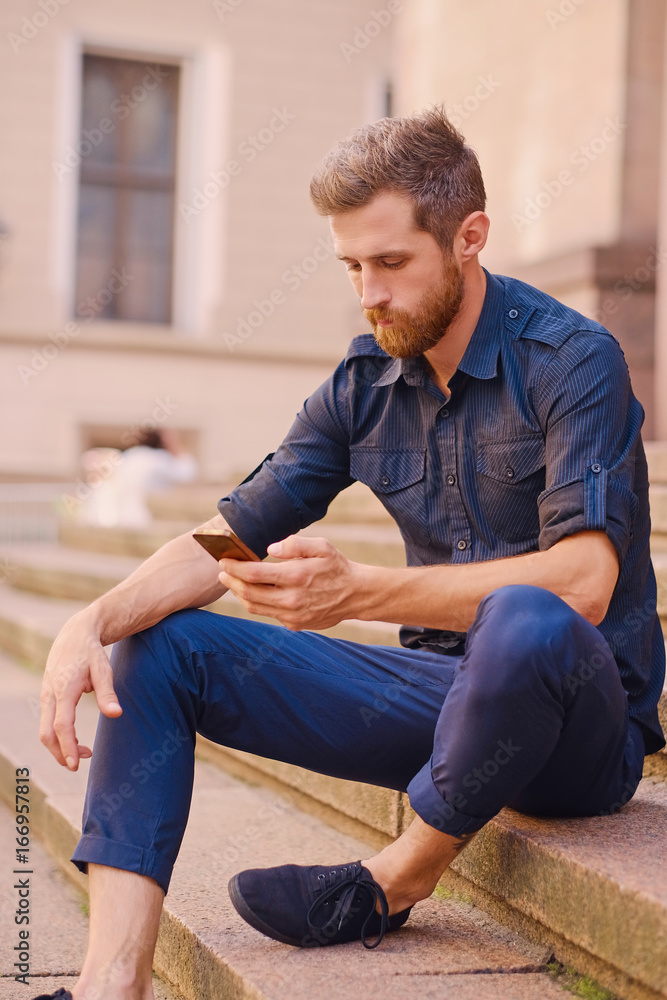 Fototapeta premium A man sits on a step and using a smartphone.