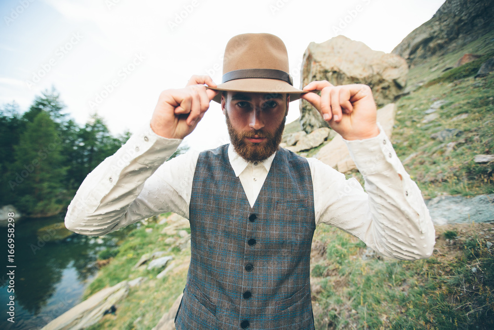 Hipster handsome male model portrait with beard wearing trendy clothes in the mountains