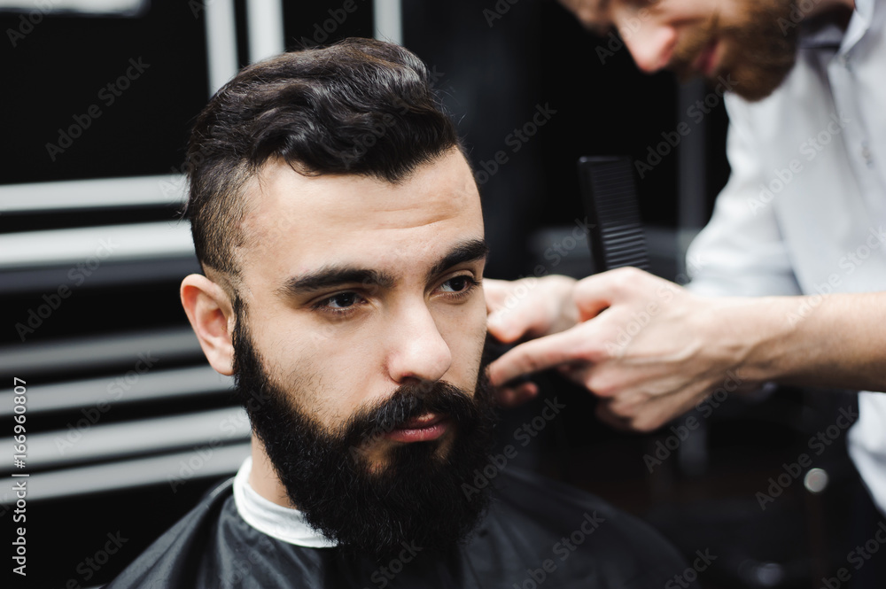Master cuts hair and beard of men in the barbershop, hairdresser makes hairstyle for a young man Master cuts hair and beard of men in the barbershop, hairdresser makes hairstyle for a young man
