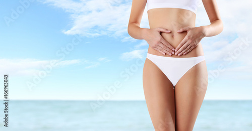 woman hands heart shape on belly, isolated on summer sea and sky background