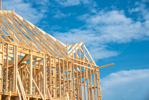 Close-up new stick built home under construction under blue sky in Humble, Texas, US. Framing structure/wood frame of wooden houses/home. House construction and real estate concept background. photo