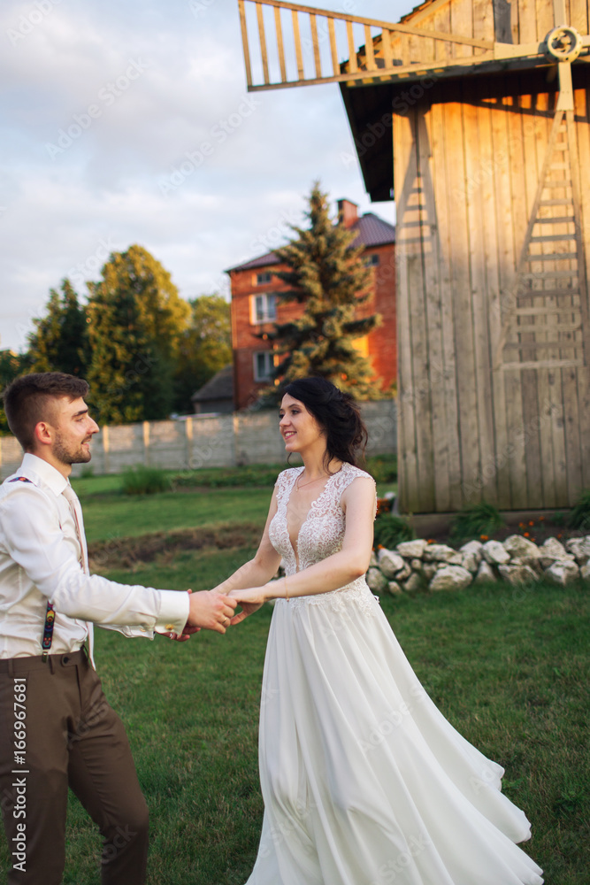 Fototapeta premium Beautiful couple holding hands and dancing near the mill