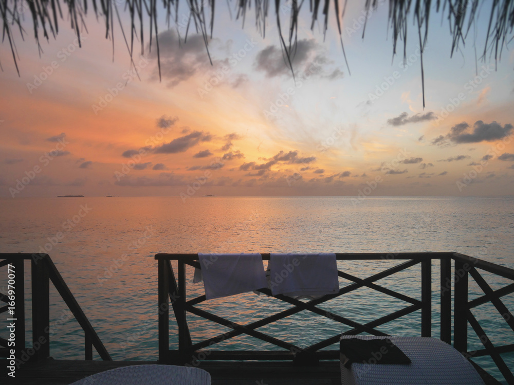Relaxing view of open sea at dawn from water bungalow room window. The image taken at Maldives tropical island resort with colorful sky in background and selective focus at distant ocean water ripples