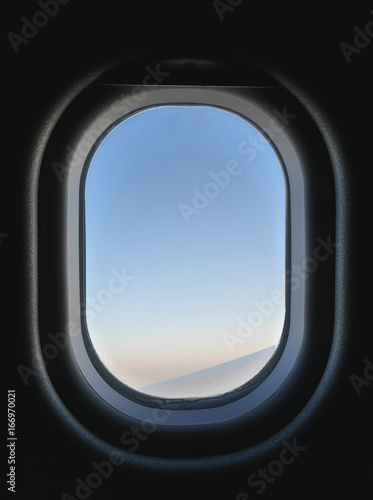 Frozen airplane window view from inside, seeing blue and pink sky and part of aircraft's wing. Inside the plane is dark, but outside is bright during day time.