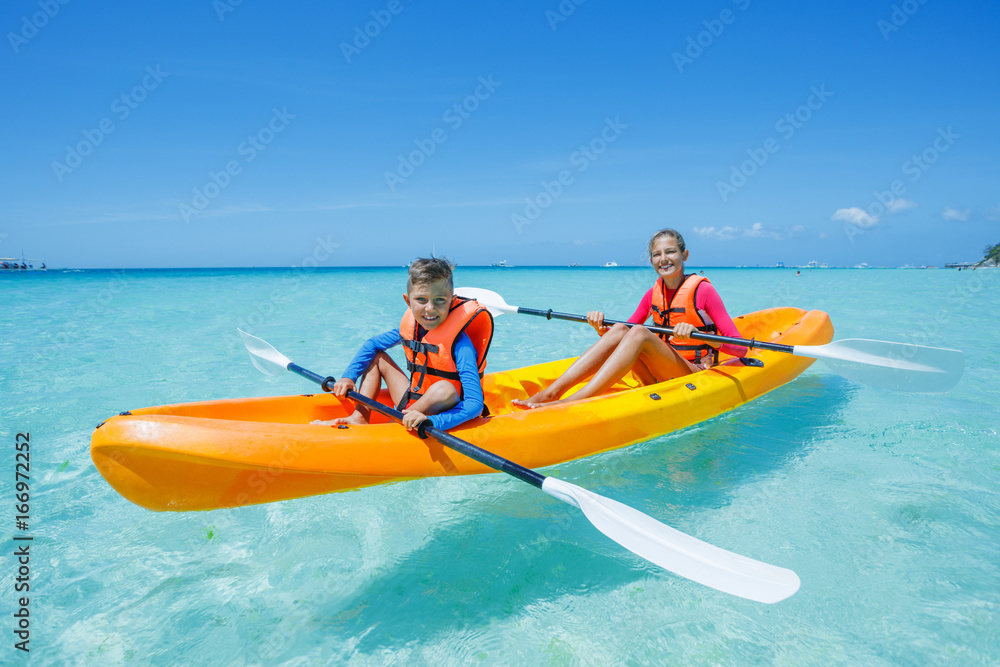 Two chirdren kayaking at tropical sea on yellow kayak