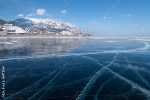 Glossy smooth surface with cracks of frozen blue ice field of lake Baikal, winter landscape photo