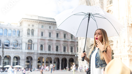 Flushed tourist girl visiting the city, with a white umbrella. Tourism and holidays theme, photo taken in Milan, Italy. © tostphoto
