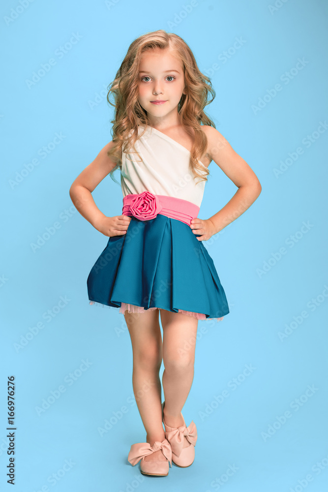 Full length of beautiful little girl in dress standing and posing over blue background Full length of beautiful little girl in dress standing and posing over blue background