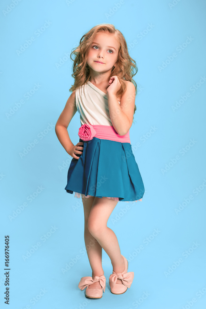 Full length of beautiful little girl in dress standing and posing over blue background Full length of beautiful little girl in dress standing and posing over blue background